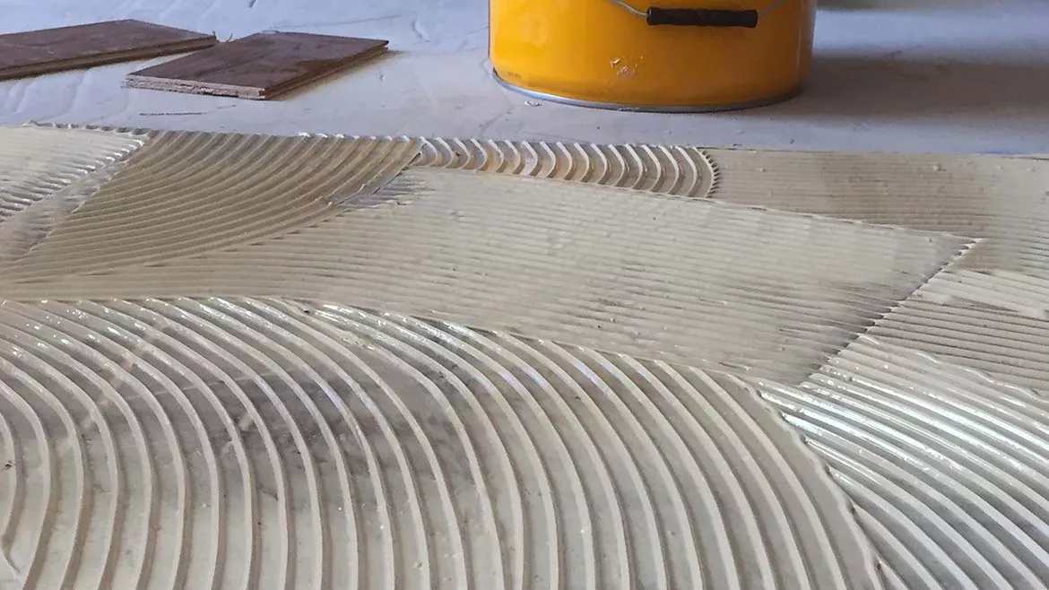 Floor adhesive with trowel ridges, wood planks, and yellow bucket.