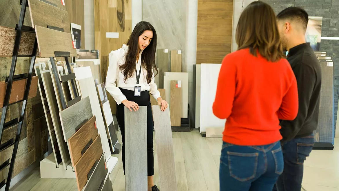 Three individuals, a man and two women, discussing flooring options while reviewing samples.